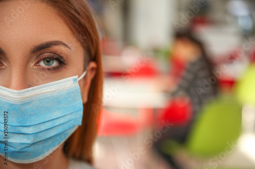 Woman with medical mask in cafe, space for text. Virus protection