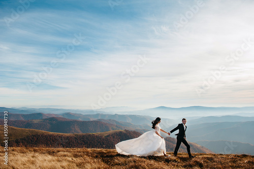 Wedding couple walks in the mountains. The groom holds the bride by the hand. Against the backdrop of a beautiful landscape
