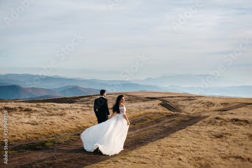 Wedding couple walks in the mountains. The bride holds the hand of the groom and looks around