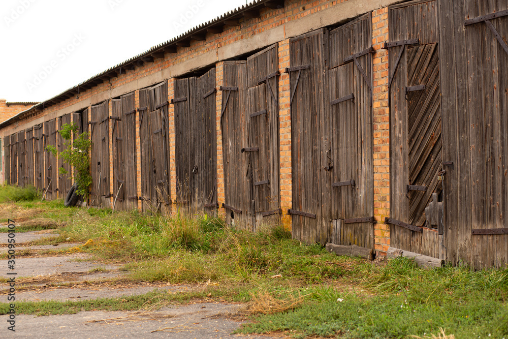 Naklejka premium Old cowshed. Large wooden gate and dried wood. Old brick building