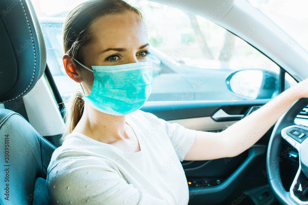 Covid-19 protection. Woman wearing protective surgical mask driving in black car looking away. Coronavirus pandemic. Prevent infection.Quarantine background with place for text. Covid-19 protection. Woman wearing protective surgical mask driving in black car looking away. Coronavirus pandemic. Prevent infection.Quarantine background with place for text.