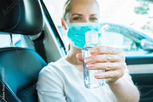 Young woman using hand sanitizer to disinfect her hands while driving a car during coronavirus outbreak. Virus prevention. Covid-19 background with copy space.