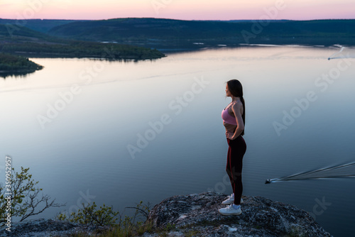 Pretty sporty girl stay on the top of the mountain and looking to the horizon with beautiful river background