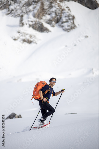 Winter sports - young man walking with snowshoes in high mountains covered with lots of snow (selective focus on the mountain in the background)