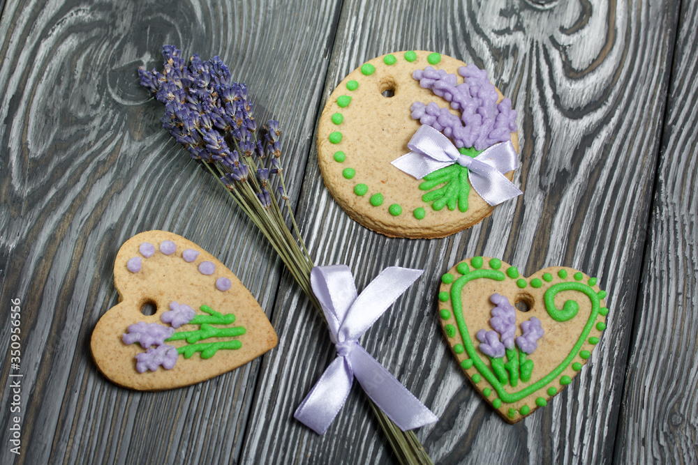 Gingerbread cookies decorated with glaze. On some ribbons tied to a bow. Gingerbread cookies are round and in the shape of a heart. Near a bouquet of lavender. On brushed pine boards.