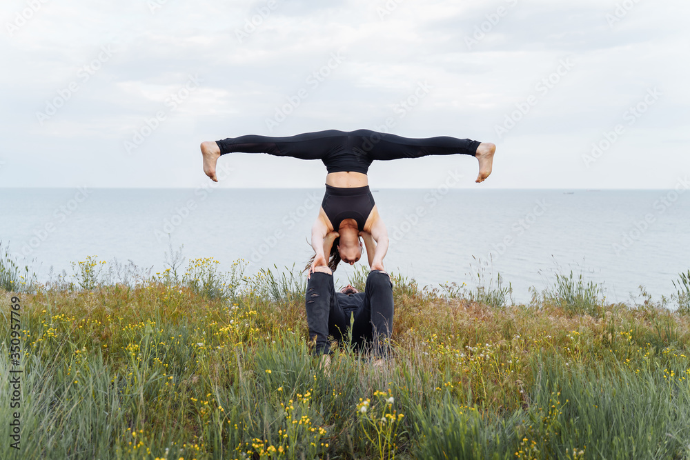 Attractive couple practicing yoga outdoors on the shore of the sea ...