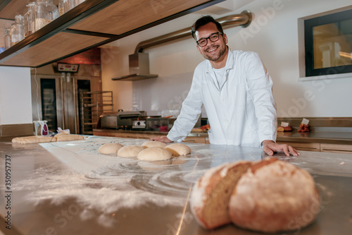 Fototapeta Young male baker preparing dough for bread in modern manufacturing