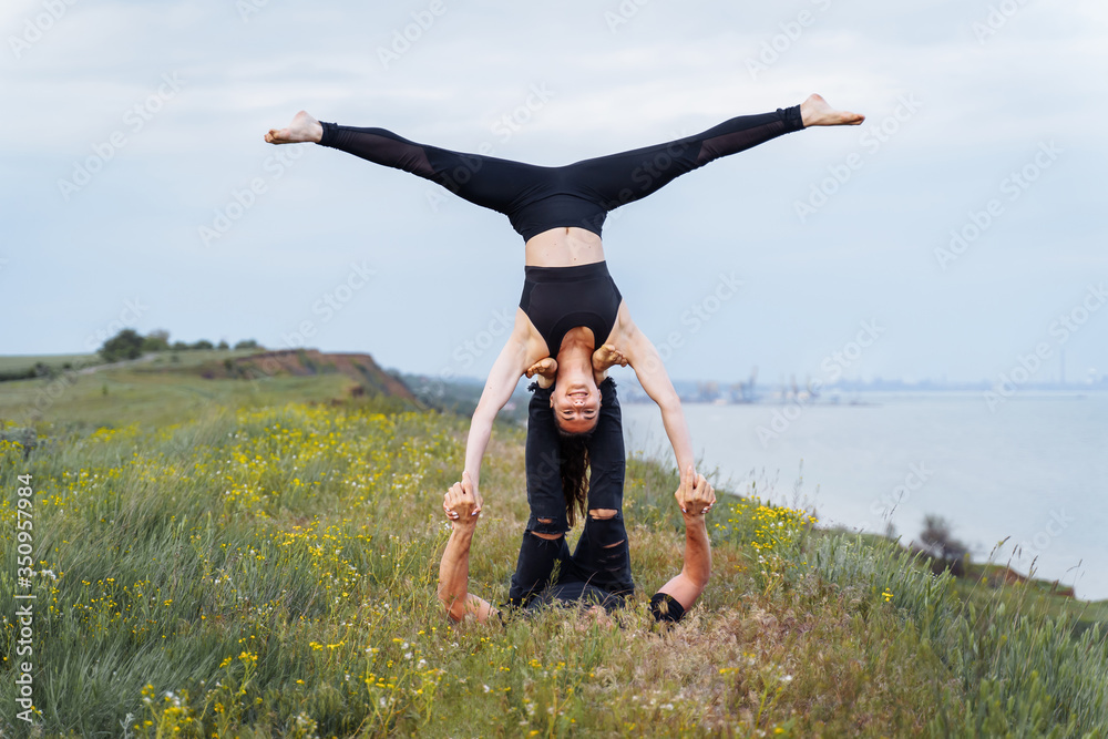 Attractive couple practicing yoga outdoors on the shore of the sea ...