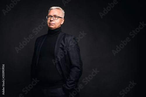 Friendly businessman wearing glasses and a suit posing with smiling at the camera against a black studio background with copy space