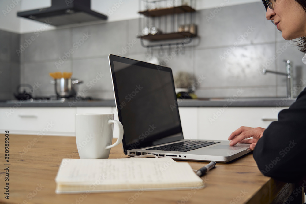 Young woman working from home during covid-19 lockdown. Woman is smartworking with laptop on kitchen table for social distance, meanwhile drinking coffee in a mug