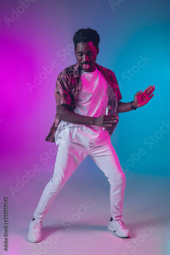 African-american male singer portrait isolated on gradient studio background in neon light. Beautiful male model with microphone. Concept of human emotions, facial expression, ad, music, art. © master1305
