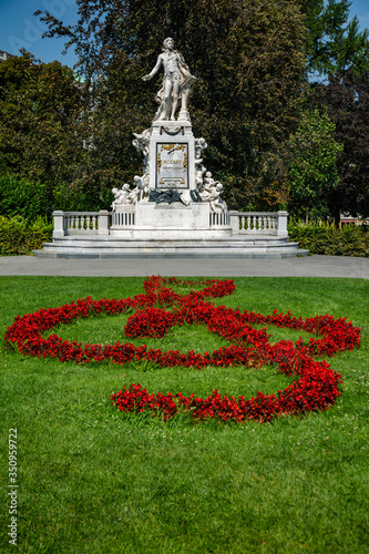 Small red flowers form musical symbols at the base of a statue for Wolfgang Amadeus Mozart entering the park in Vienna, Austria