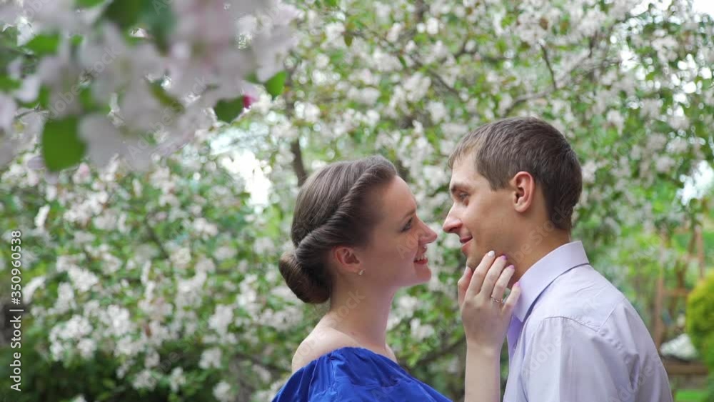 Loving Young Man and Woman Talking in a Spring Park. They Enjoying Time Together over Blooming Apple Trees. Concept of Spring, Love, Togetherness and Romantic Relationships Loving Young Man and Woman Talking in a Spring Park. They Enjoying Time Together over Blooming Apple Trees. Concept of Spring, Love, Togetherness and Romantic Relationships
