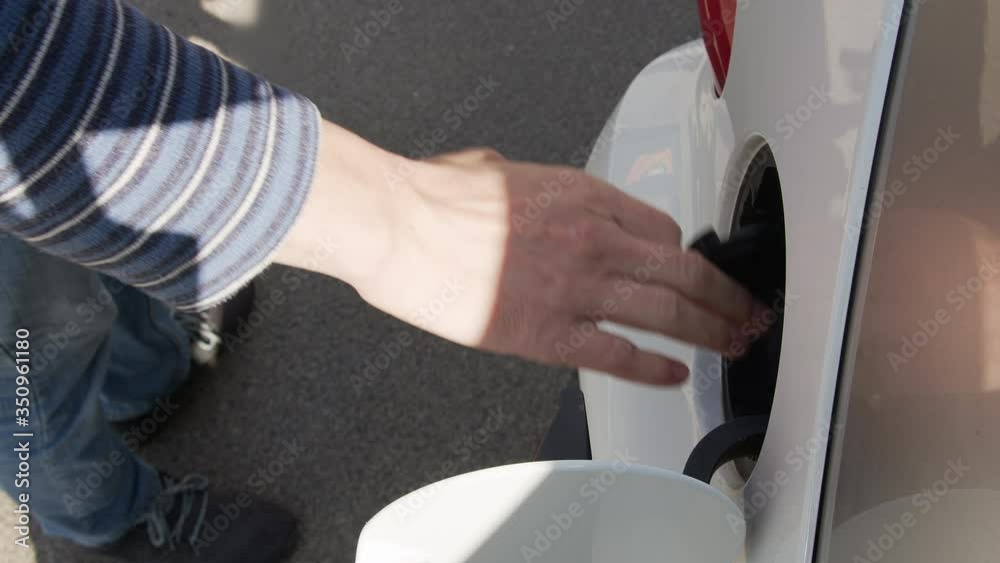 Man's hand inserts the charging cable to charge the electric car. Charging an electric car at a gas station. Man's hand inserts the charging cable to charge the electric car. Charging an electric car at a gas station.
