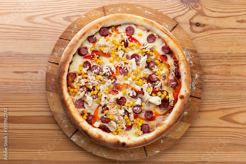 hearty italian pizza on a wooden board. crispy cheese pizza with hunting sausages, pepper, chicken and corn