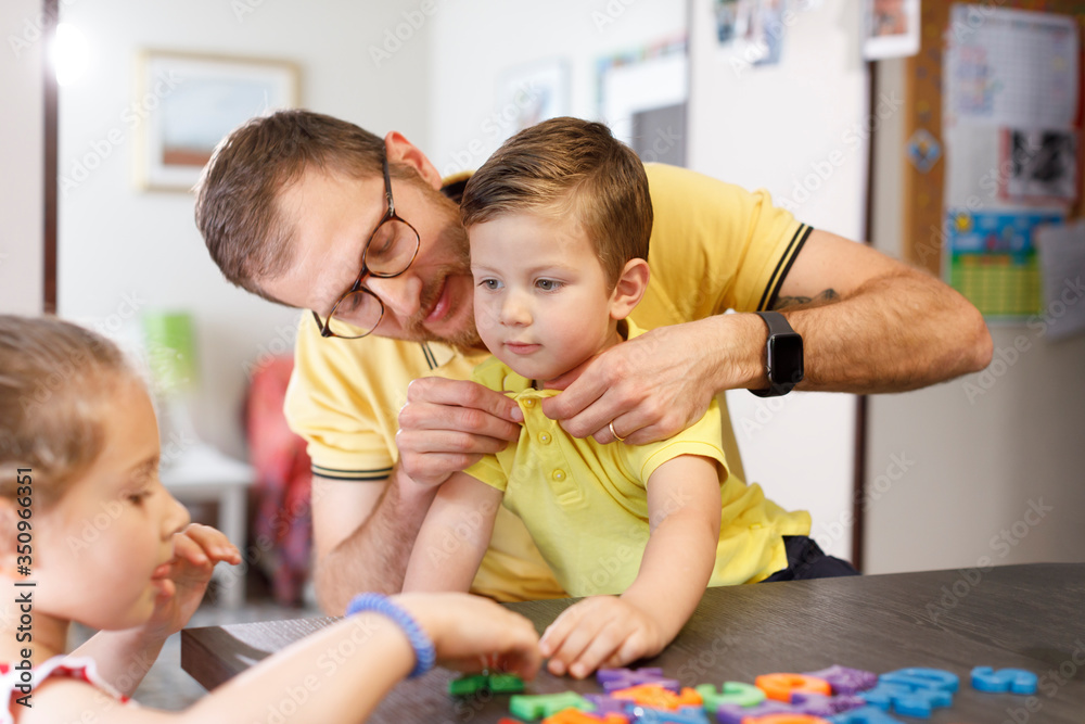 Fototapeta premium papà aiuta il figlio a mettersi la polo gialla come la sua in contesto familiare