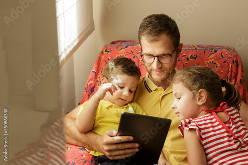 padre usa il tablet con i 2 figli seduti nel divano di casa