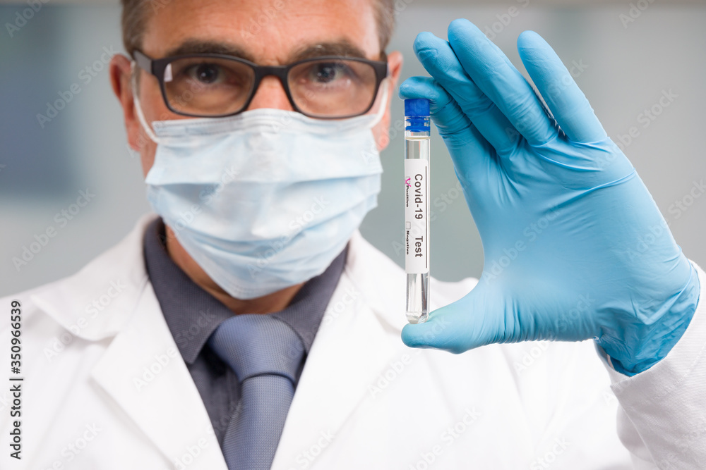 Scientist or doctor with medical face mask and medical gloves is handling virus test tube with result markers in front of laboratory in background Scientist or doctor with medical face mask and medical gloves is handling virus test tube with result markers in front of laboratory in background