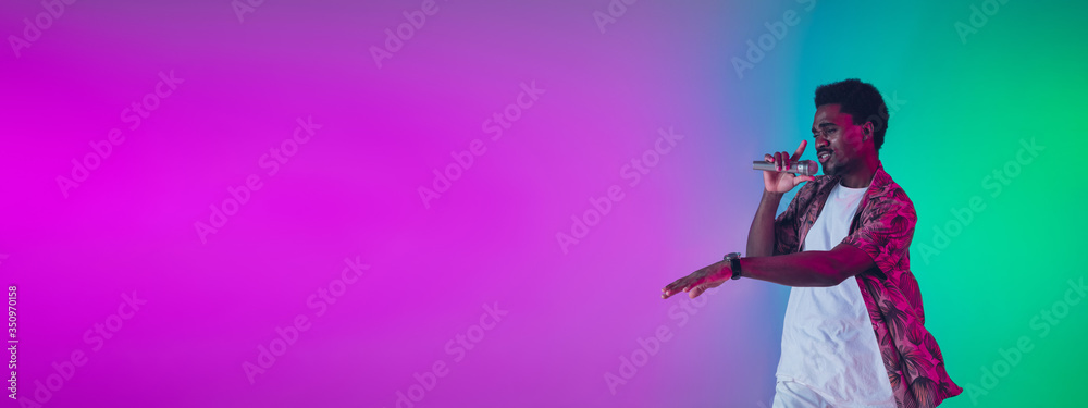 African-american male singer portrait isolated on gradient studio background in neon light. Beautiful male model with microphone. Concept of human emotions, facial expression, ad, music, art. African-american male singer portrait isolated on gradient studio background in neon light. Beautiful male model with microphone. Concept of human emotions, facial expression, ad, music, art.