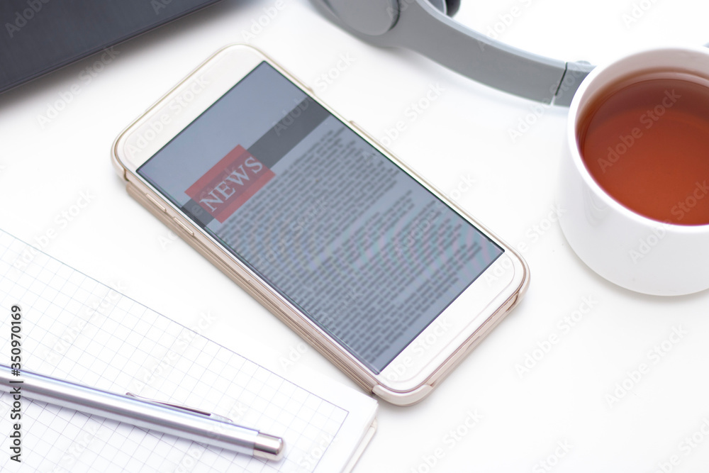 Online news on a mobile phone. Close up of smartphone screen with news feed on a white table. Mock up site. Newspaper Online news on a mobile phone. Close up of smartphone screen with news feed on a white table. Mock up site. Newspaper