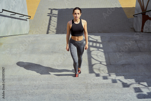Fototapeta Naklejka Na Ścianę i Meble -  sportive young brunette woman walking on stairs. Beautiful fitness girl in stylish sportswear outdoors. sport and healthy lifestyle concept.