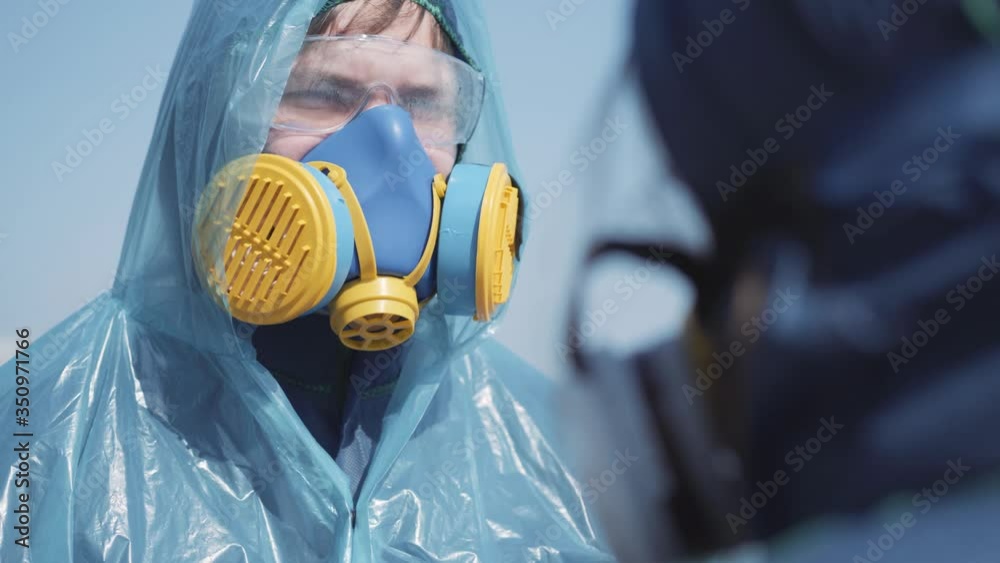 People dressing each other in biohazard suits outdoors. Portrait of ...