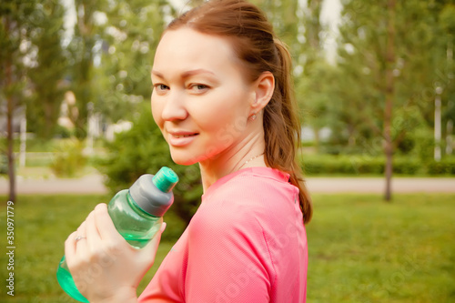 Active sporty woman holding bottle after training outdoors