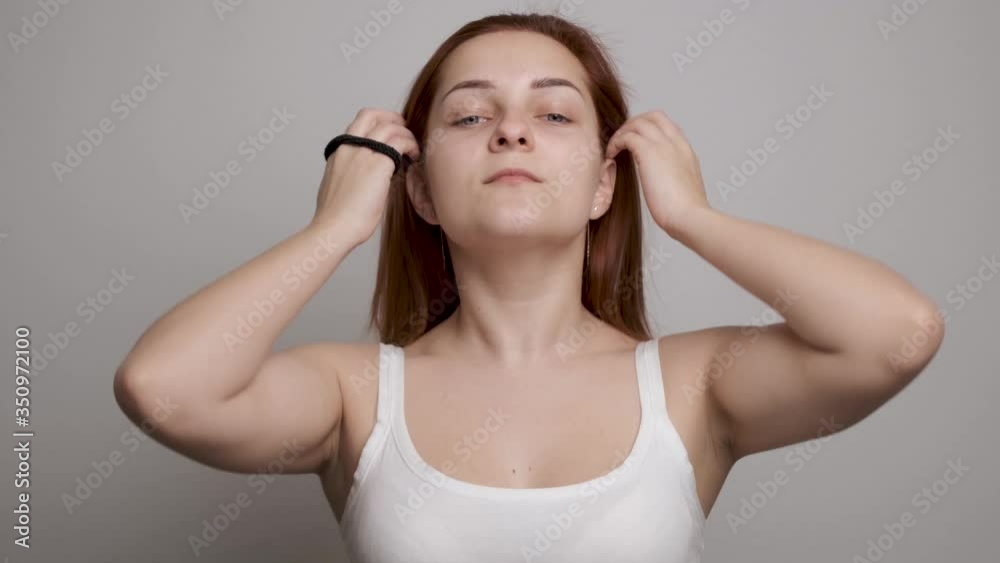 Young beautiful woman doing hair style looking in mirror, smiling girl make ponytail hairstyle in bathroom or bedroom in the morning getting ready during everyday routine at home. Grey background Young beautiful woman doing hair style looking in mirror, smiling girl make ponytail hairstyle in bathroom or bedroom in the morning getting ready during everyday routine at home. Grey background