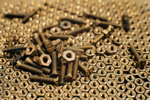 Close-up, macro. Old Soviet brass countersunk head screws with a flat head screwdriver. Texture, background of brass nuts laid out in the form of honeycombs. Gold color screws. Dirty wood screws in oi