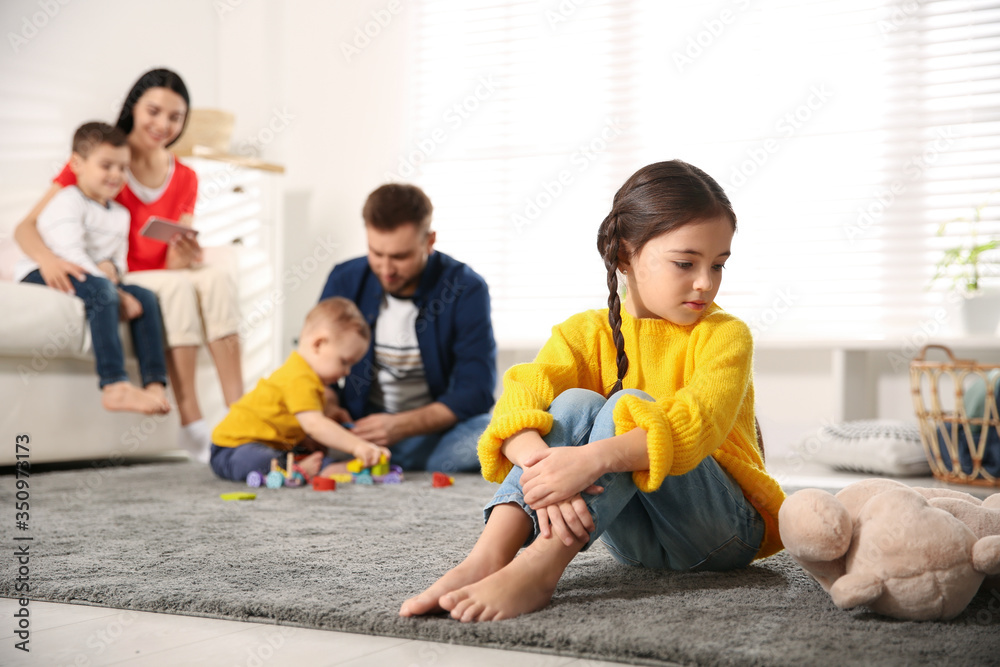 Unhappy little girl feeling jealous while parents spending time with other children at home Unhappy little girl feeling jealous while parents spending time with other children at home