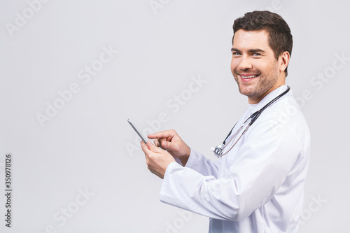 Portrait of a cheerful smiling medical doctor or nurse with stethoscope using pc tablet computer and looking at camera isolated on white background.