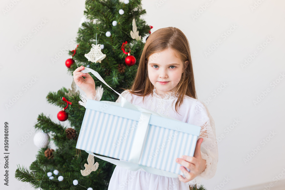 Child girl opens gift box near Christmas tree. Holidays, christmas time and presents concept. Child girl opens gift box near Christmas tree. Holidays, christmas time and presents concept.