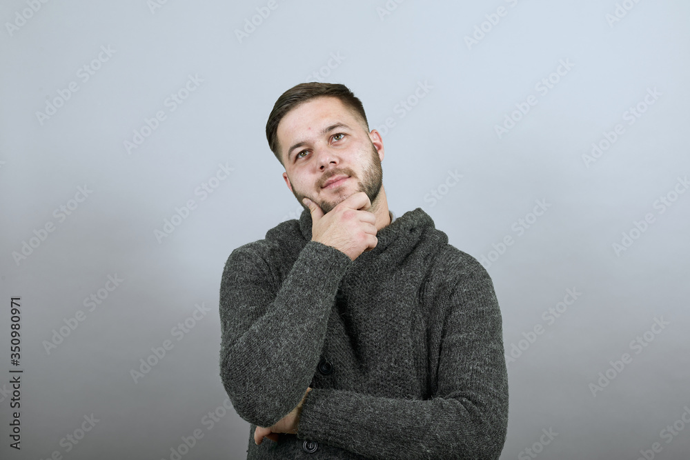 Young Bearded Dark Haired Man In Black Stylish Shirt On Gray Background, Dreamy Male Holds Hand Over His Beard And Thinks. Concept Of The Smart People Are Intellectuals Young Bearded Dark Haired Man In Black Stylish Shirt On Gray Background, Dreamy Male Holds Hand Over His Beard And Thinks. Concept Of The Smart People Are Intellectuals
