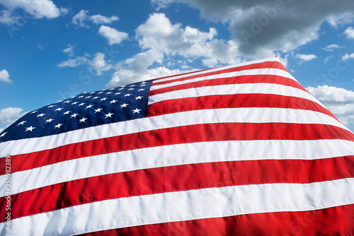 Closeup of American flag blowing in wind, blue sky white clouds