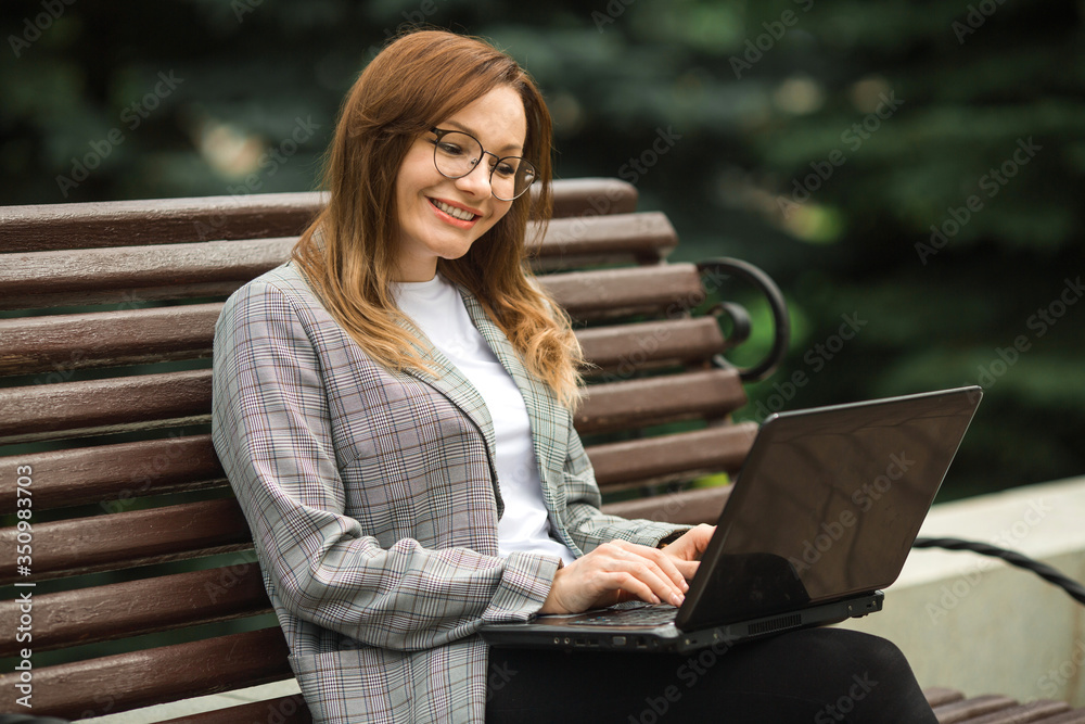 beautiful young woman in a gray jacket with a laptop in the park sitting on a bench beautiful young woman in a gray jacket with a laptop in the park sitting on a bench