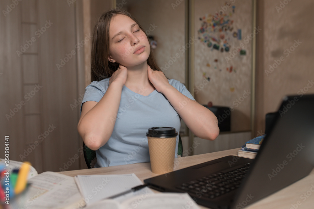 Tired kneading neck, muscle pain, teenager girl 12-15 years old, rest after hard lesson, home laptop. E-education and distance learning Internet and video communications. A cup of coffee with tea. Tired kneading neck, muscle pain, teenager girl 12-15 years old, rest after hard lesson, home laptop. E-education and distance learning Internet and video communications. A cup of coffee with tea.