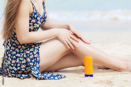 Hand of female holding sunscreen applying sunscreen on her hands from a bottle on the beach with the sea /Health concepts and skin care.