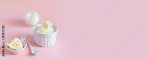 Fotografie Tasty rice milk porridge with banana in white mask and milk in milkman on pink b