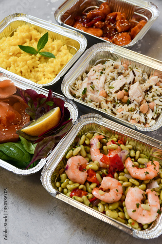 Food delivery. Different aluminium lunch box with healthy natural food risotto, chicken chickpeas and rice, salmon salad, hot chicken teriyaki, shrimp and green beans. airlines food. airline meals