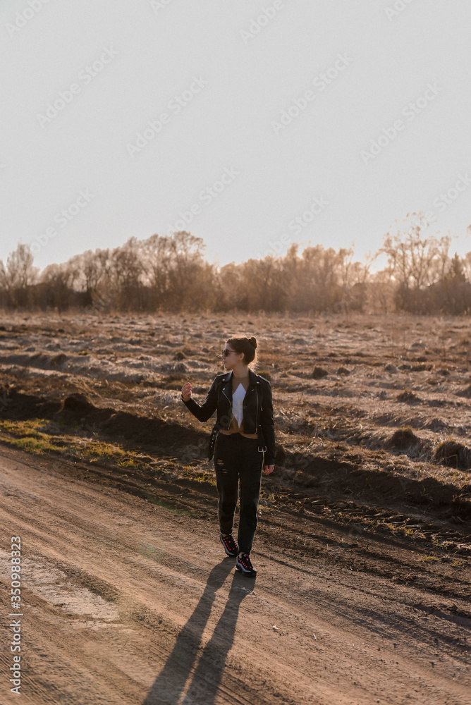 Young girl walking on a dirt road in nature. A young woman in a leather jacket in nature Young girl walking on a dirt road in nature. A young woman in a leather jacket in nature