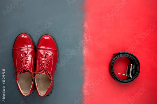 Style. Top view of classic red patent leather shoes and black leather belt for trousers on red and grey background.