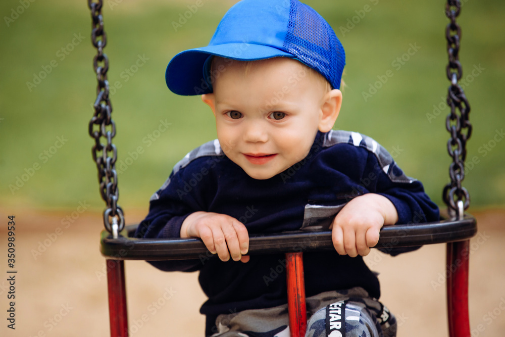 Funny and handsome boy rejoices, rides on a children's swing, plays on the playground, 1-2 years Funny and handsome boy rejoices, rides on a children's swing, plays on the playground, 1-2 years