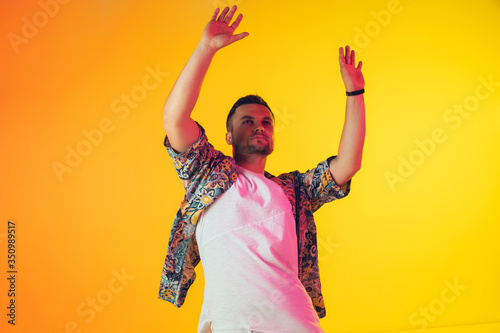 Young caucasian musician in casual dancing on gradient yellow background in neon light. Concept of music, hobby, festival. Joyful party host, DJ, stand upper, dancer. Colorful portrait of artist.
