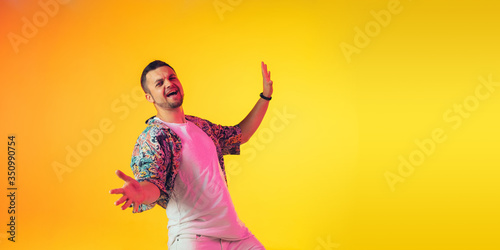 Young caucasian musician in casual dancing on gradient yellow background in neon light. Concept of music, hobby, festival. Joyful party host, DJ, stand upper, dancer. Colorful portrait of artist.