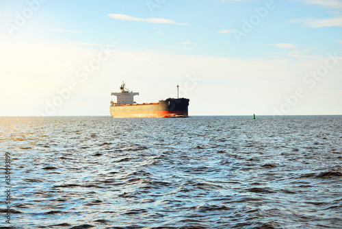 Large bulk carrier (cargo ship) sailing in an open sea from Europoort. Clear blue sky with cirrus clouds. Rotterdam, Netherlands. Global communications, logistics, industry theme photo