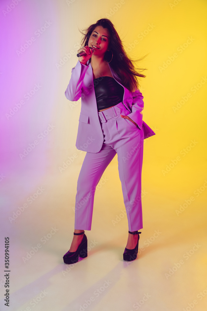 Caucasian female singer portrait isolated on gradient studio background in neon light. Beautiful female model in pink wear with microphone. Concept of human emotions, facial expression, ad, music, art Caucasian female singer portrait isolated on gradient studio background in neon light. Beautiful female model in pink wear with microphone. Concept of human emotions, facial expression, ad, music, art