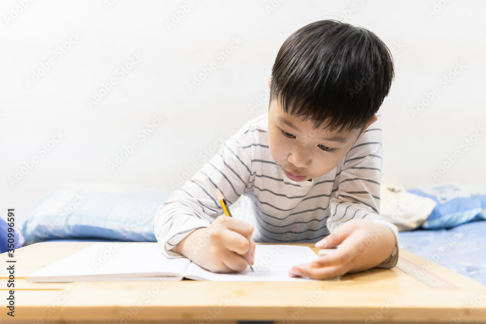 Home school and new normal lifestyle concepts.Asian boy studying through online media and do homework at home due to social distance policy to prevent the spread of the coronavirus(Covid-19) Home school and new normal lifestyle concepts.Asian boy studying through online media and do homework at home due to social distance policy to prevent the spread of the coronavirus(Covid-19)