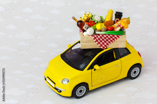 A yellow toy car delivering food, drinks and grocery. Online food shopping or donation concept.