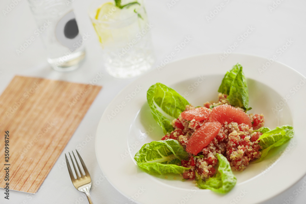 lettuce, quinoa, grapefruit fillet and bell pepper in a white plate, next to water with lemon