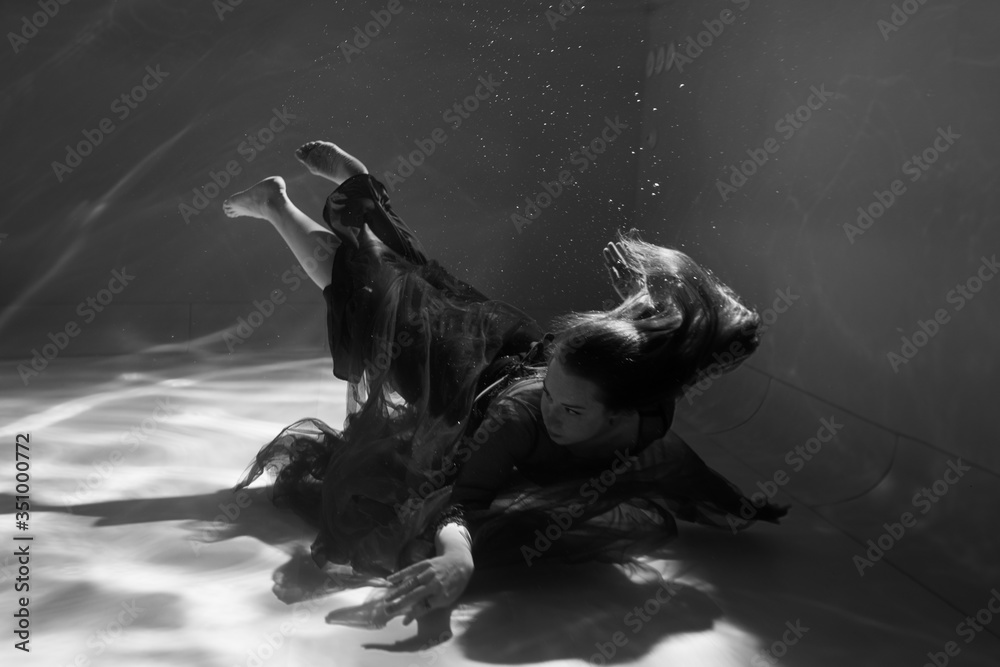 Black and white photo. Beautiful girl underwater in a red dress swims in the pool. Tenderness and elegance. Bubbles and a lot of water Black and white photo. Beautiful girl underwater in a red dress swims in the pool. Tenderness and elegance. Bubbles and a lot of water